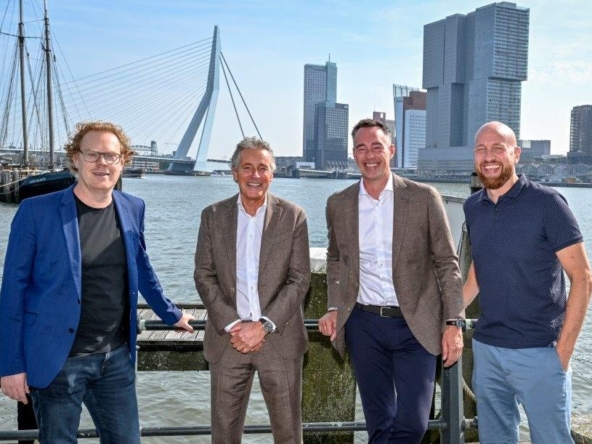 Vier Männer in lockerem Business-Dress stehen vor der Skyline von Rotterdam.